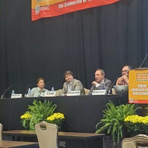 Jen Gregory, Executive Director, Southern Tier 8 Regional Board; Jimmy Carr, CEO, All Points Broadband; Aaron Deacon, Managing Director, KC Digital Drive, Kansas City; and Bob Knight, President and CEO, Harrison Edwards PR, sitting at a table with Deacon speaking. 