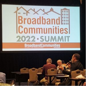 A county administrator from rural Michigan asks panelists a question under a projection reading Broadband Communities 2022 Summit; Broadband Communities Magazine: Building a Fiber-Connected World. 